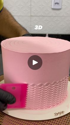 a pink cake is being cut with a large plastic knife on top of the cake