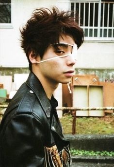 a young man with glasses and a leather jacket is standing in front of a building