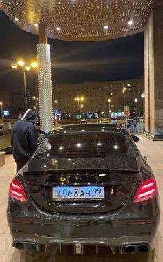 a man standing next to a black car in front of a gas station at night