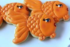 decorated cookies with orange icing and blue eyes on a white table top, including one cookie shaped like a fish