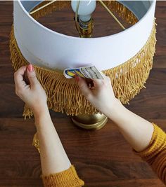 two hands are reaching for a book under a table lamp that has fringed tassels on it