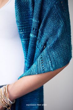 a woman wearing a blue knitted cardigan and bracelets, with her hand on her hip