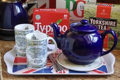 a blue tea pot sitting on top of a plate next to cups and saucers