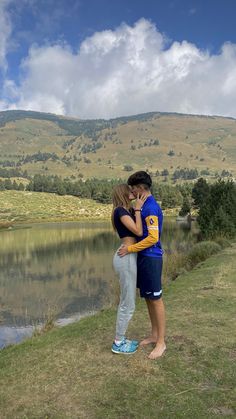 a man and woman standing next to each other near a lake with mountains in the background