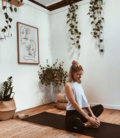 a woman sitting on a yoga mat in front of a wall with potted plants