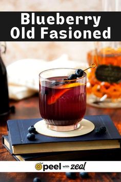 a blueberry old fashioned drink in a glass on top of a book