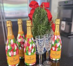 four bottles of champagne and two glasses on a table with a red bow around it