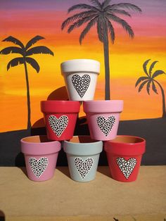 several pots with hearts painted on them in front of a painting and palm trees,