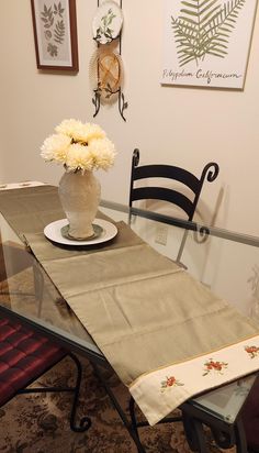 a vase with flowers sitting on top of a table next to a chair and wall hangings