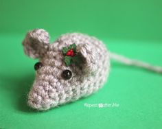 a crocheted mouse with holly leaves on it's head sitting on a green surface