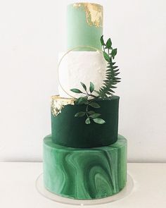 a three tiered green and gold wedding cake with greenery on the top layer