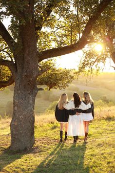 three women standing in front of a tree with the sun shining down on their backs