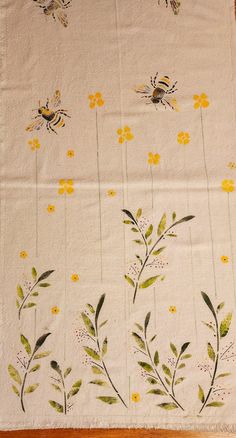 a table cloth with yellow flowers and bees on white fabric, sitting on a wooden floor