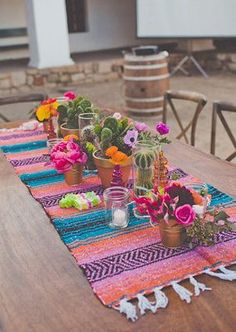 the table is set with colorful flowers and vases on it, along with an old barrel