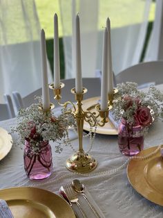 the table is set with candles and flowers in vases, plates and silverware