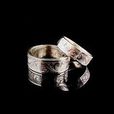 two silver rings sitting next to each other on a black surface with the reflection of them