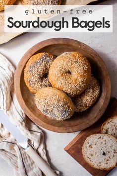 several bagels in a wooden bowl next to a knife and napkin on a table