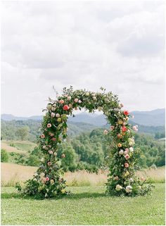 an arch made out of flowers on top of a lush green field with mountains in the background