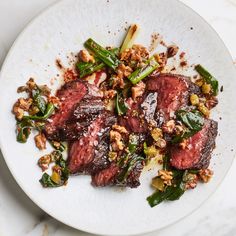 a white plate topped with meat and veggies on top of a marble table