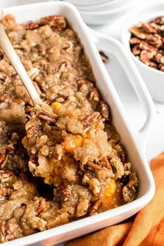 a white casserole dish filled with granola and topped with pecans next to two bowls of oatmeal