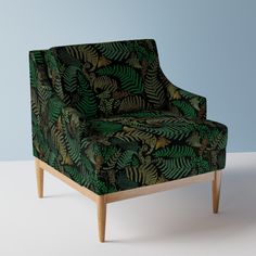 a green chair sitting on top of a white floor next to a blue wall and wooden legs