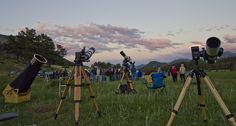 several telescopes set up in the grass with people looking at them and taking pictures behind them