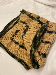 a crocheted blanket laying on top of a white bed with green and black trim