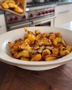 a white bowl filled with cooked potatoes on top of a wooden table next to an oven