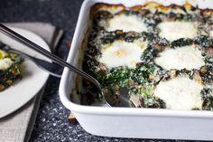 a casserole dish with spinach and eggs in it on a table next to a fork