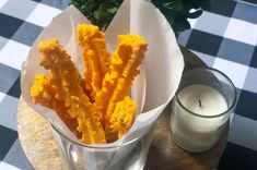 a glass vase filled with cheetos sitting on top of a table next to a candle