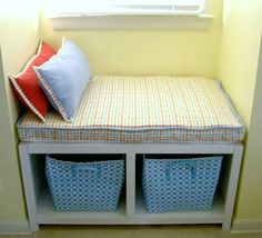 a white bench with two blue baskets underneath it and a red pillow on the seat