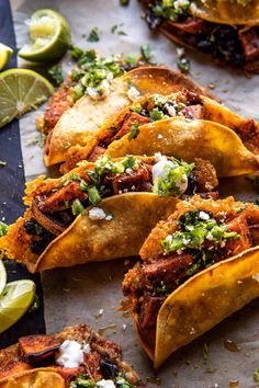 several tacos with toppings and lime wedges on the side, ready to be eaten