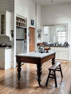 a kitchen with white walls and wooden floors has an island table in front of the refrigerator