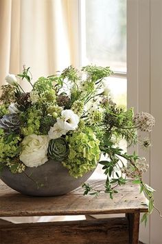 a vase filled with flowers sitting on top of a wooden table next to a window