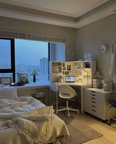 a bedroom with a bed, desk and window overlooking the cityscape in the distance