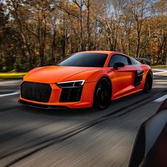 an orange sports car driving down the road with trees in the backgrouund