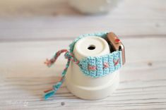 a white cup with a blue crocheted cover on it and a camera inside