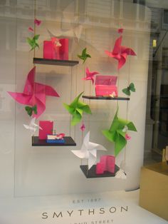 origami birds hanging from shelves in a store window with pink and green boxes