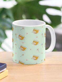 a coffee mug sitting on top of a wooden table next to a book and phone