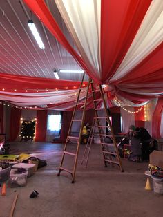 a room with red and white draping on the ceiling, ladders in front of it