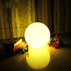 a white light sitting on top of a table next to flowers and books in front of a wooden wall