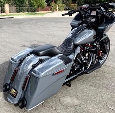 a silver motorcycle parked on the street next to a parking lot with trees in the background