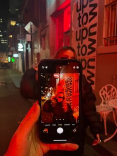 a person holding up a cell phone in front of a building with red lights on it