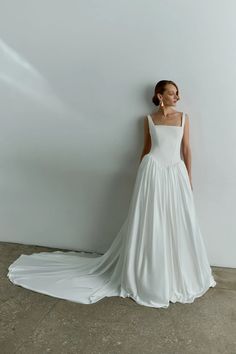 a woman in a white wedding dress standing against a wall with her back to the camera