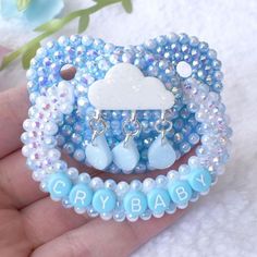 a hand holding a blue and white beaded bracelet with clouds, raindrops and beads