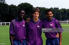 three soccer players pose for a photo in purple uniforms on the field with trees in the background