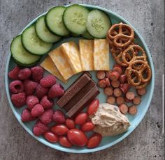 a plate full of food including crackers, cucumbers, raspberries and chocolate