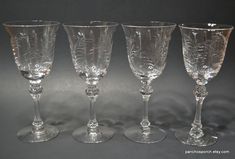 four clear wine glasses sitting next to each other on a gray surface with white background