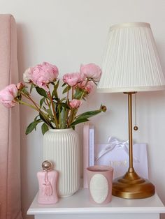 pink flowers are in a white vase next to a lamp and other items on a table