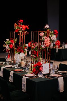 the tables are set up with black linens and red floral centerpieces on them